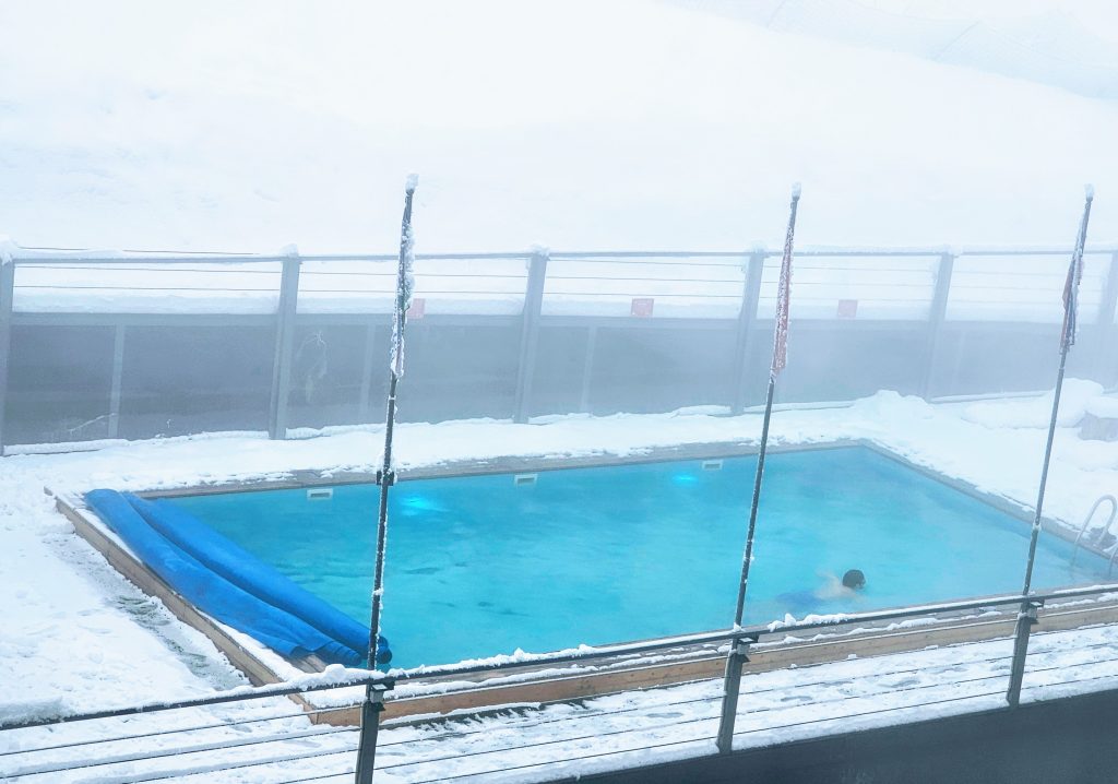 Heated outdoor pool at Shymbulak Ski Resort in Kazakhstan with snowy mountains in the background.