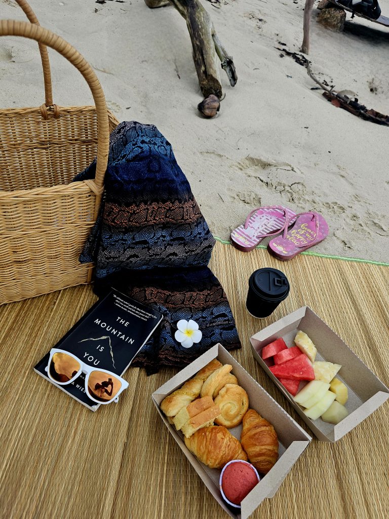 Picnic basket with fruits, pastries,  coffee and a book on the private beach at Berjaya Langkawi.