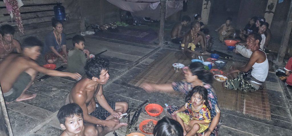 Dinner scene with the Mentawai family gathered on the wooden floor inside the uma.