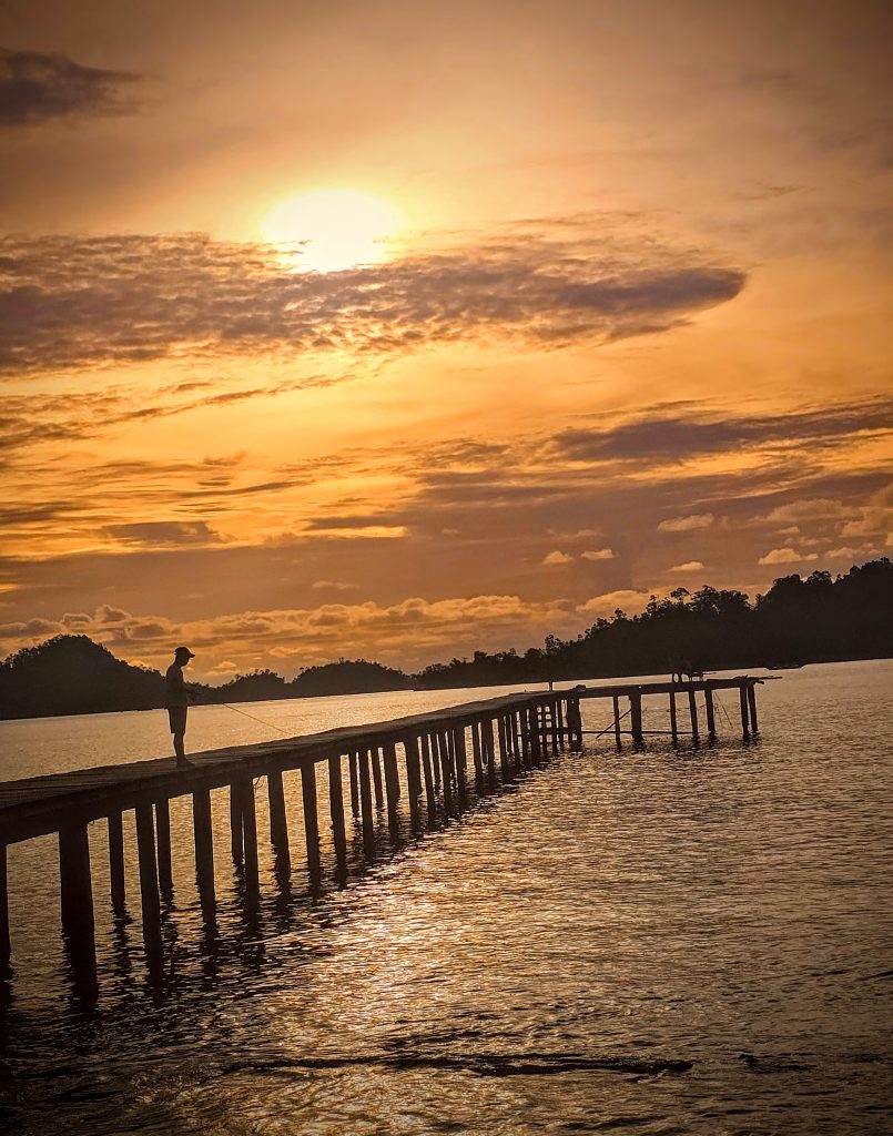 Local man fishing from the jetty at sunset in Sungai Pinang, West Sumatra