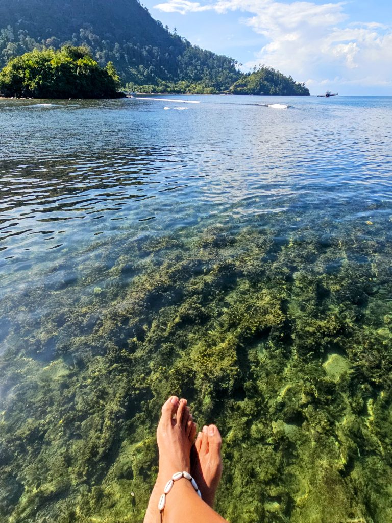 Feet dangling over crystal clear water at the jetty of Ricky's Beach House in West Sumatra