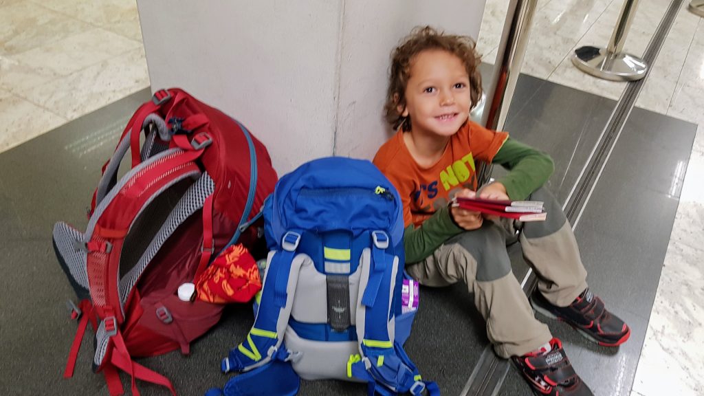 Three year old boy sitting on the airport floor beside a rucksack while waiting at immigration and travelling light
