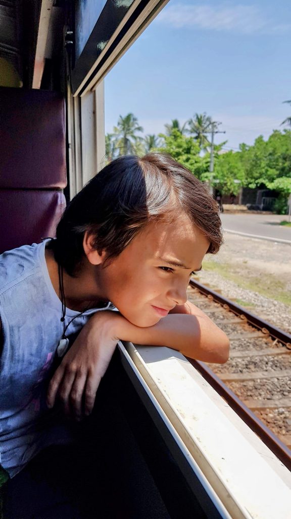 Boy travelling light looking out of a train window in Sri Lanka