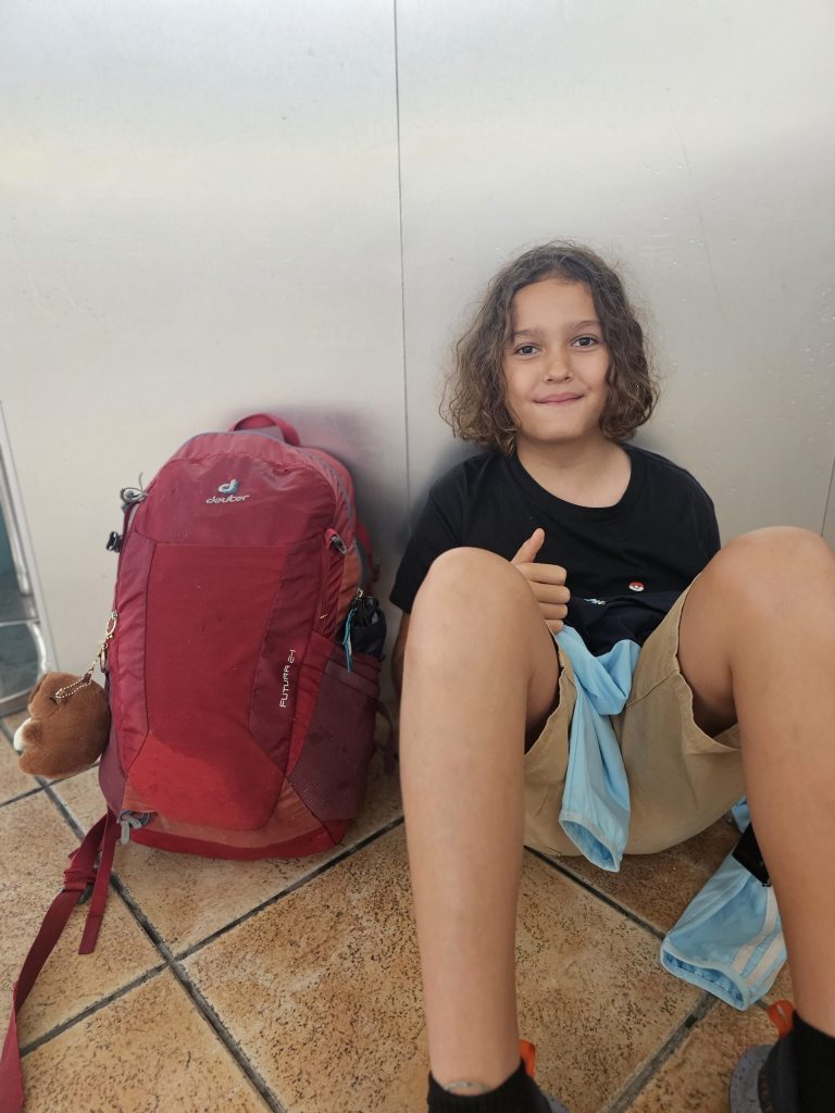 Young boy sitting on the floor at a train station beside his rucksack while travelling light